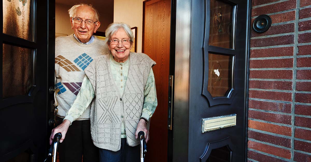 An elderly man and a woman standing next to each other in doorway of home