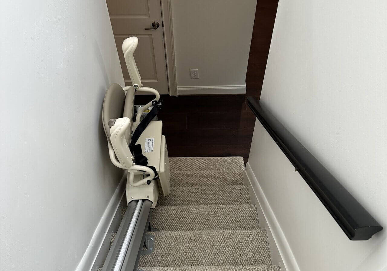 Staircase with a stairlift installed on the left side, leading down to a closed door.